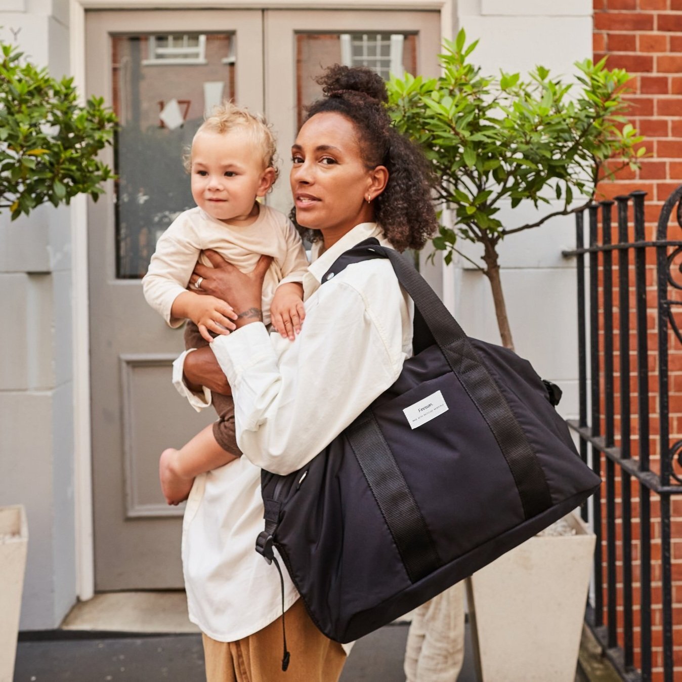 FINNSON IDA HOLDALL BLACK MODEL WEARING ON SHOULDER HOLDING BABY