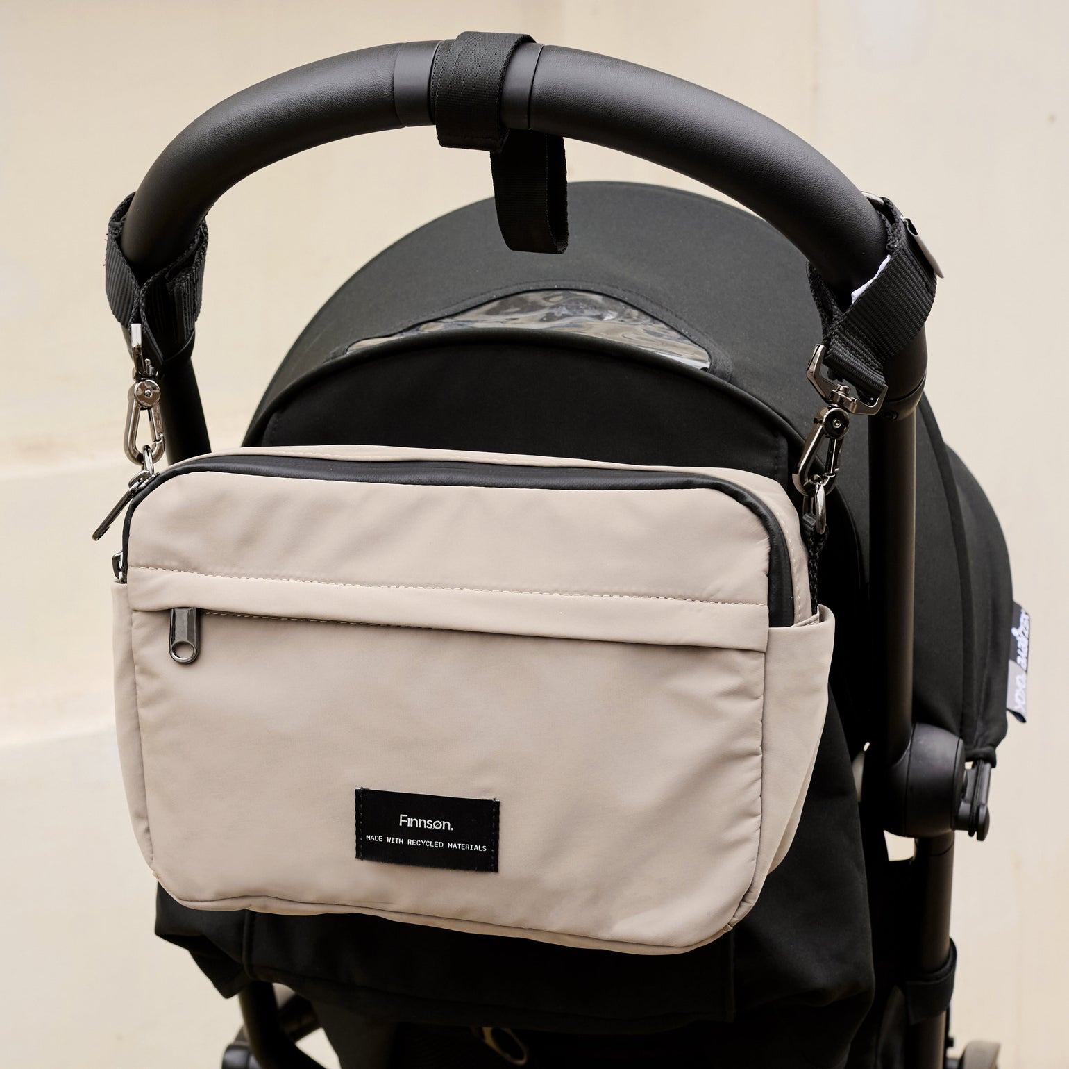 Frida taupe diaper bag attached to a black stroller on a beige background