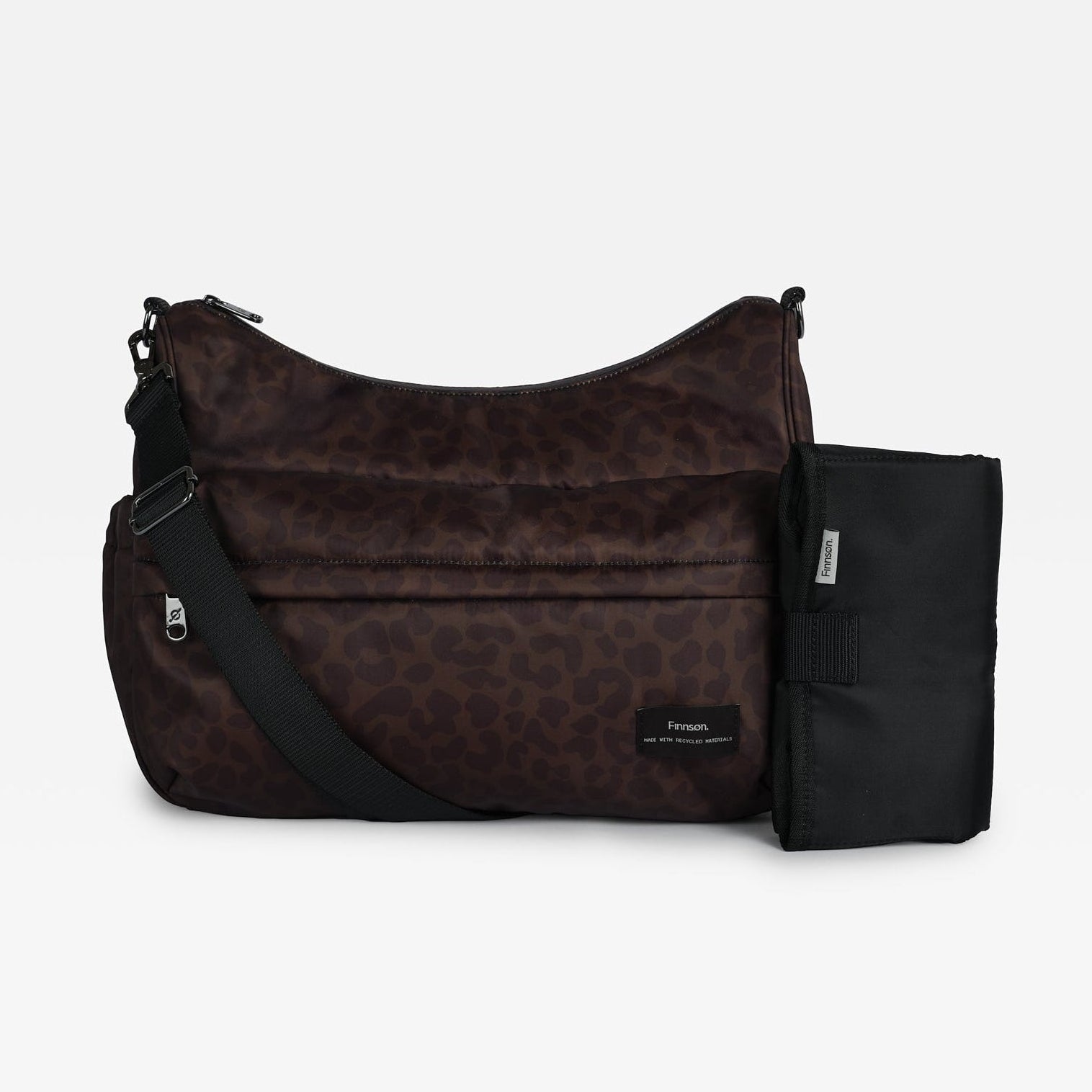 The Clara changing bag in chocolate leopard with a black strap and a black changing mat, displayed against a solid light gray background.