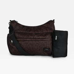 The Clara changing bag in chocolate leopard with a black strap and a black changing mat, displayed against a solid light gray background.