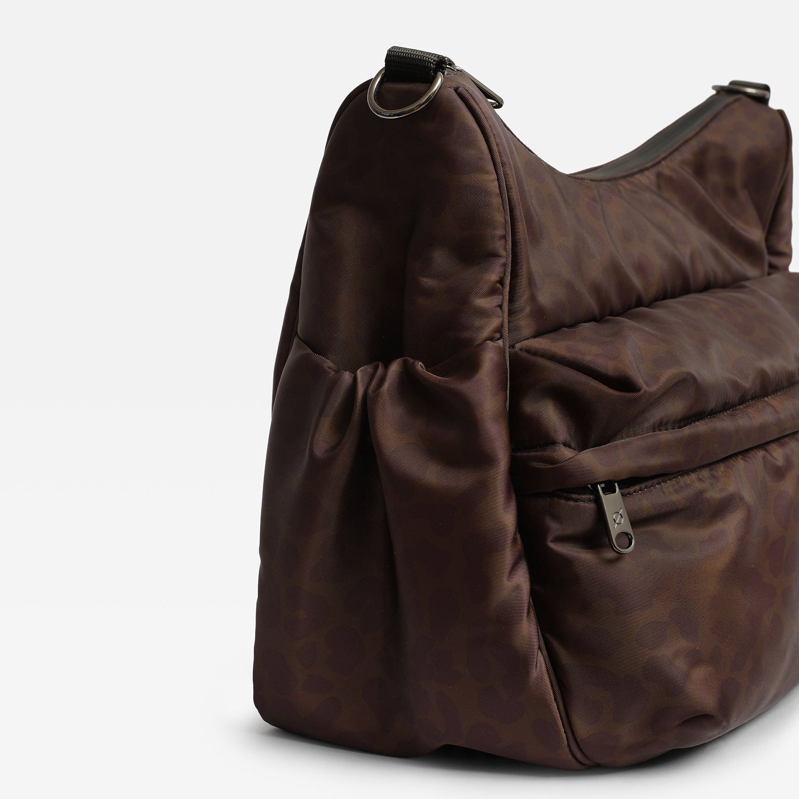 Clara chocolate brown leopard nylon shoulder bag with a slouchy, padded design, a front zippered pocket, and a side drawstring detail, photographed on a light gray background.