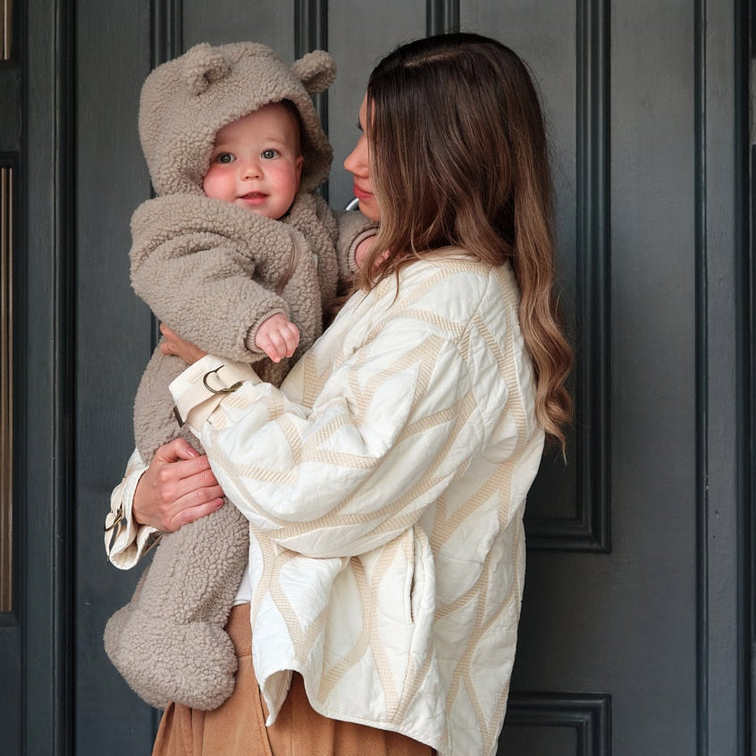 Woman holding a child in front of a house door wearing Alf borg beige eco pram suit