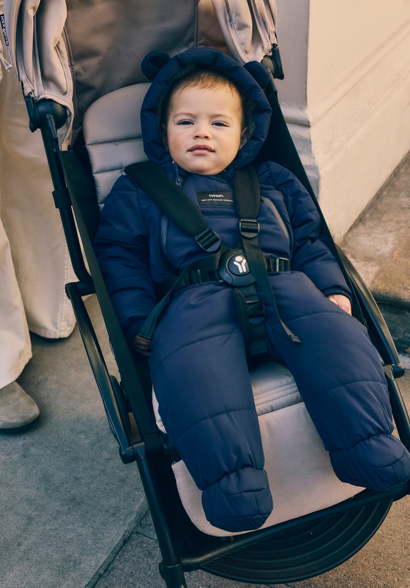 Child in Anders navy snowsuit sitting in a stroller on a sidewalk.