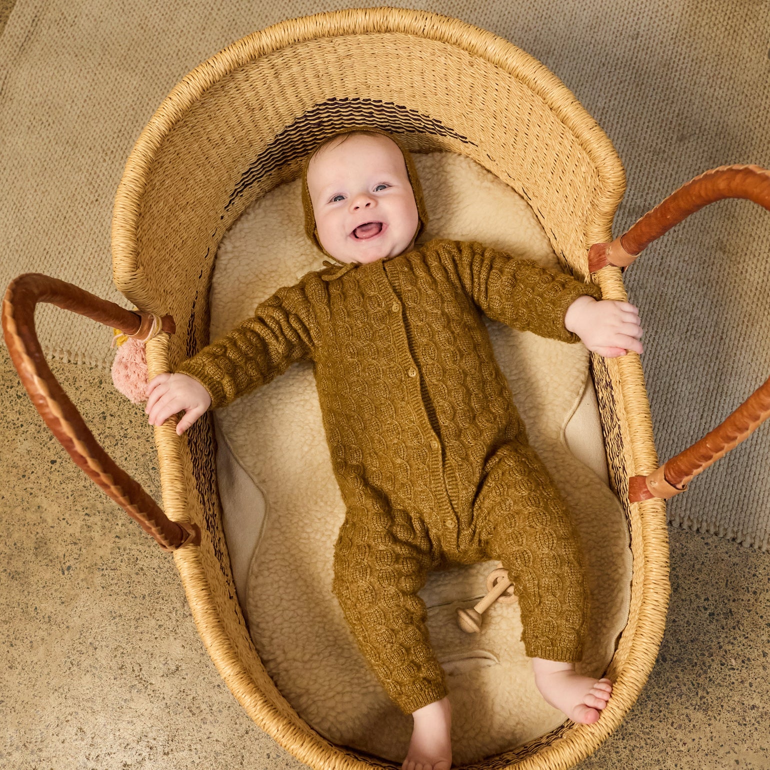 Baby in a brown outfit lying in a wicker basket on Astor beige wool liner 