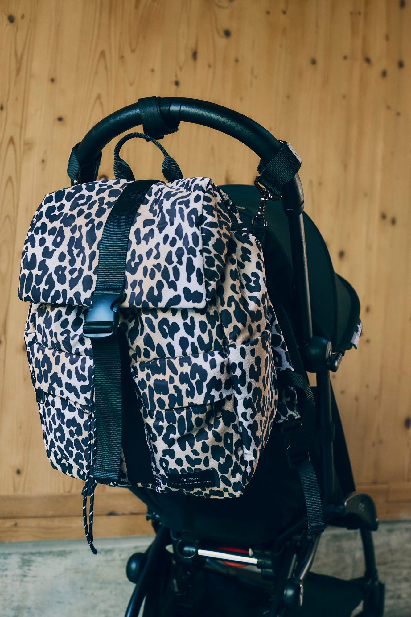 Elise Leopard print changing backpack attached to a stroller against a wooden background
