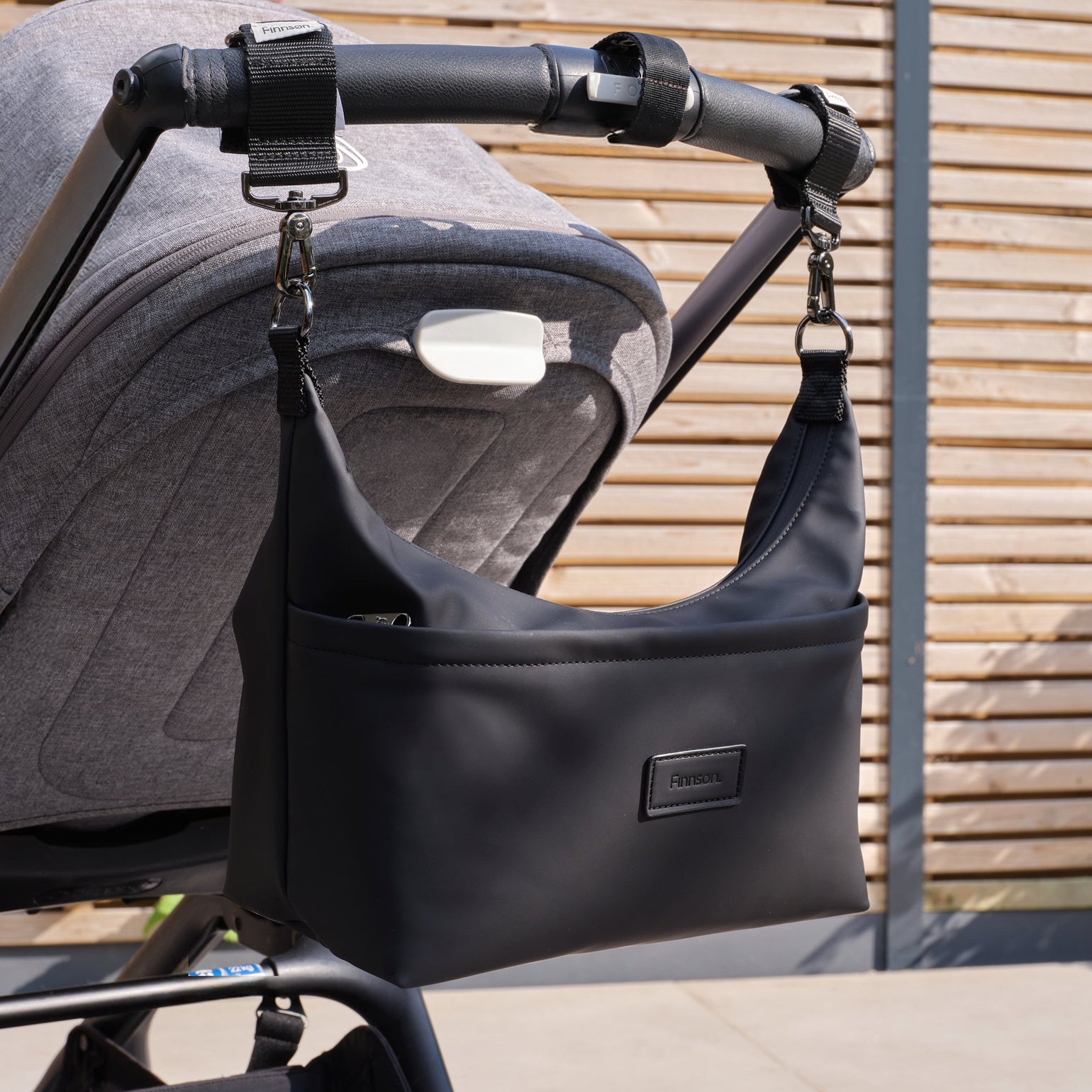 Fia black stroller organiser attached to a stroller against a wooden fence.