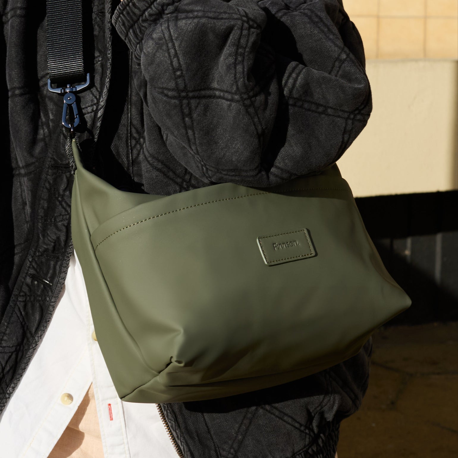 Person holding a Fia khaki stroller organiser bag against a beige wall
