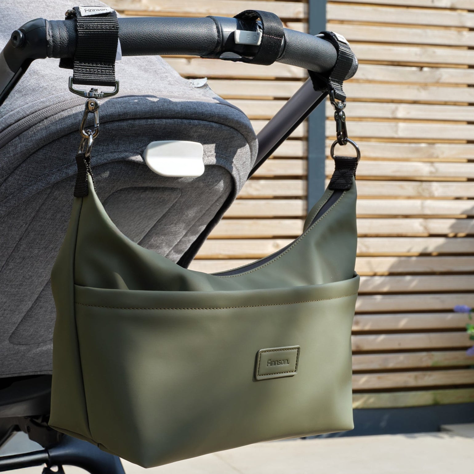Fia khaki stroller organiser bag attached to a stroller with a wooden background