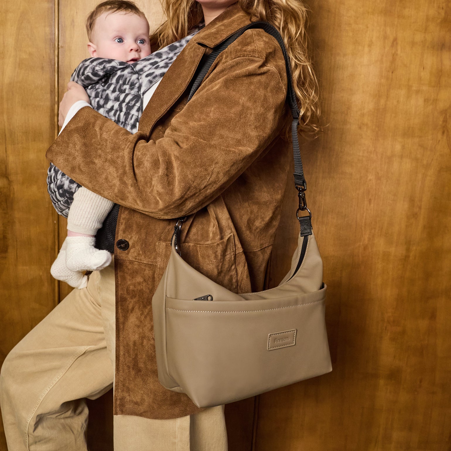Woman holding a baby in a sling with a fia mocha stroller organiser against a wooden background