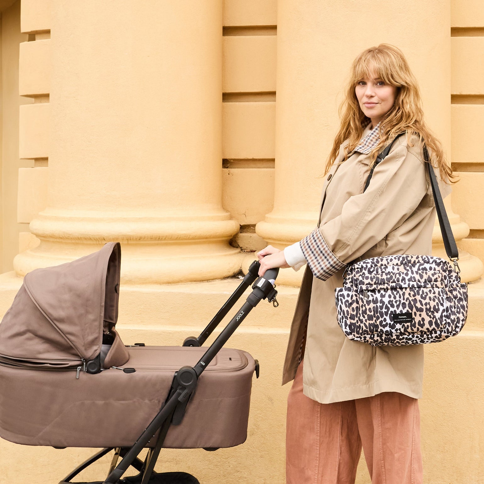 Woman pushing a baby stroller with the Freya leopard print bag, standing against a beige wall.