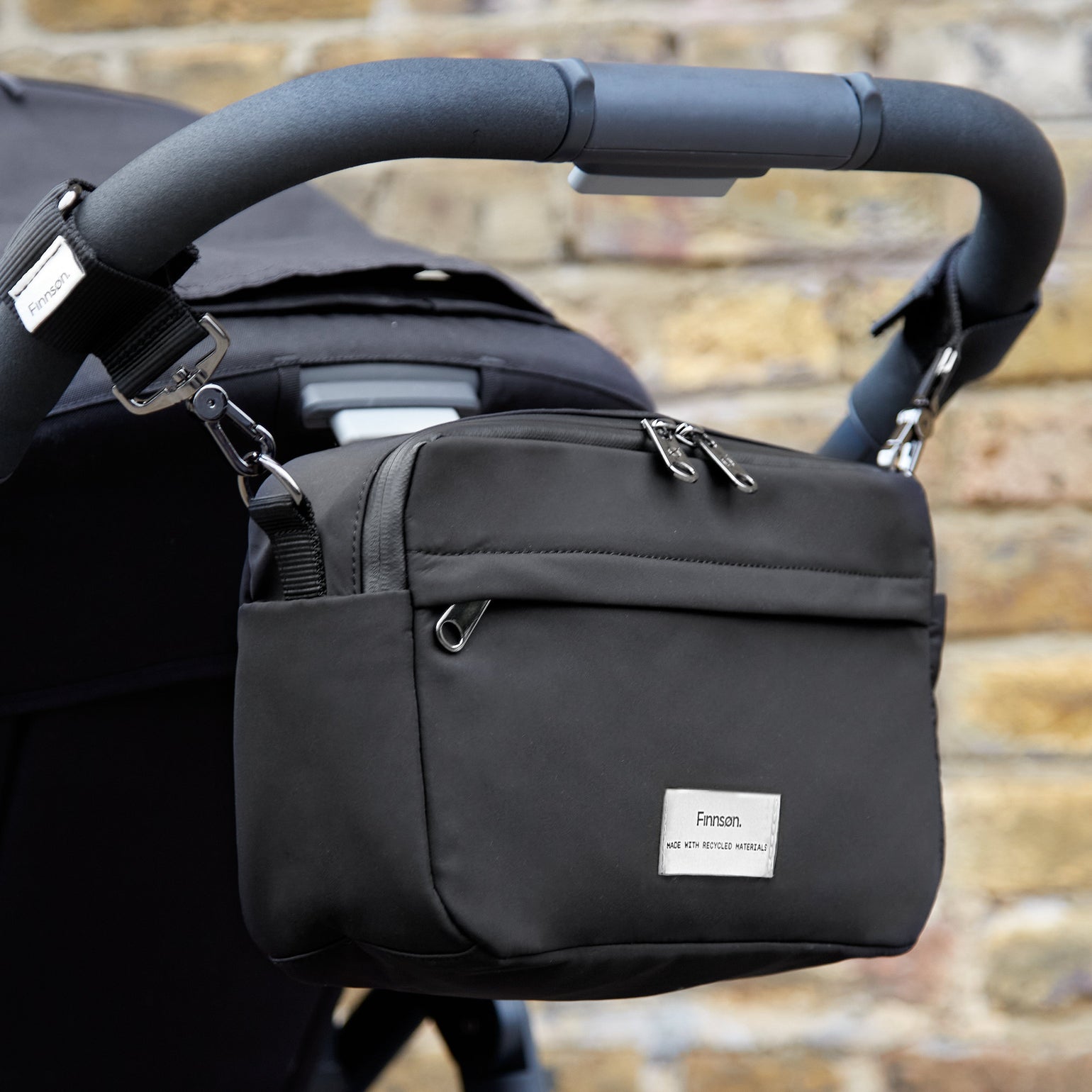 Frida eco stroller organiser on back of black pram against a brick wall