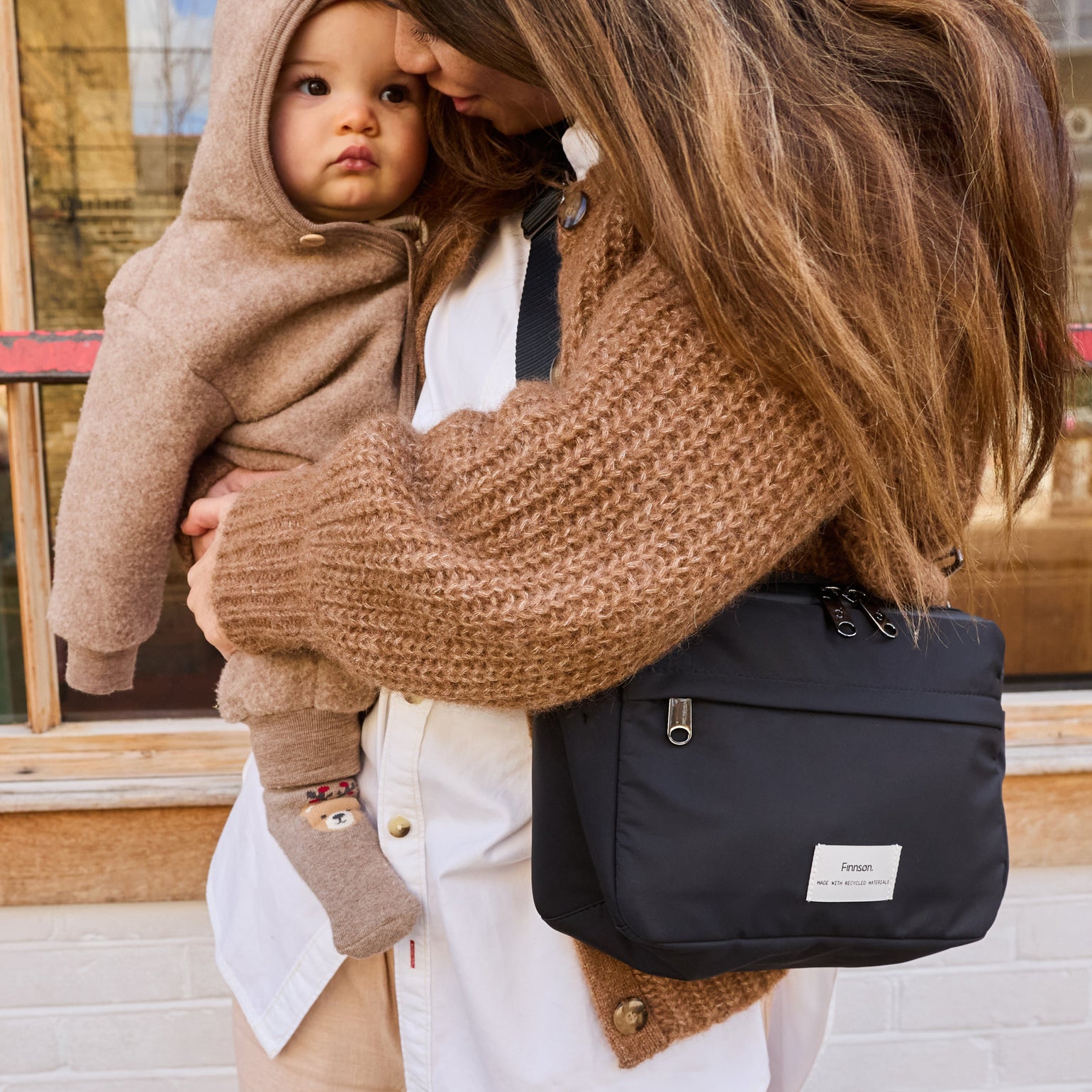 Frida eco stroller organiser in black being worn on a lady who is carrying a baby 