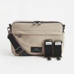 A taupe Frida stroller organiser with a comfortable crossbody strap and stroller clips, featuring multiple pockets with a grey interior, designed for easy access.
