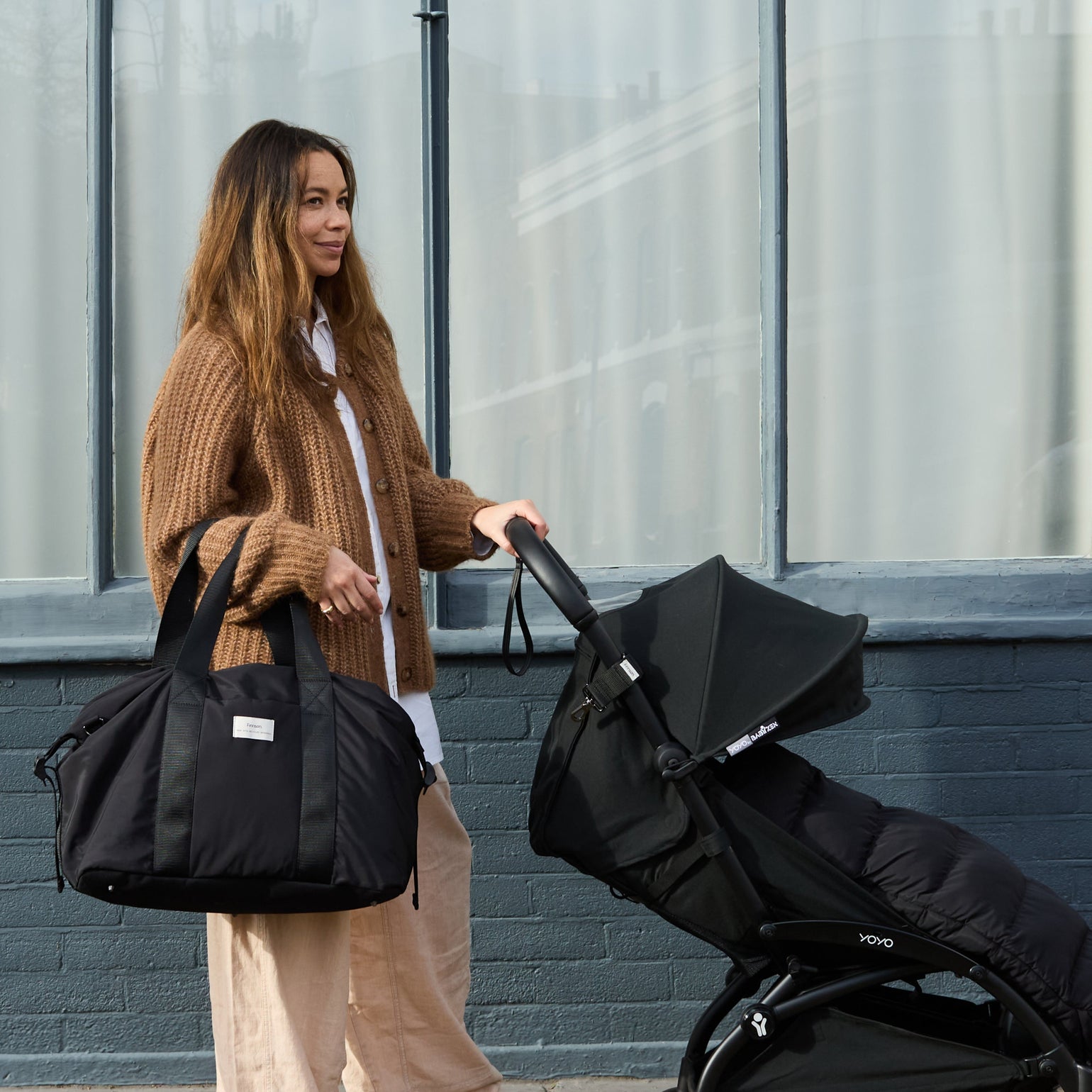 IDA Black Eco Holdall Changing Bag carried over the shoulder while a parent pushes a stroller, showcasing its spacious holdall design and practical style for everyday outings.