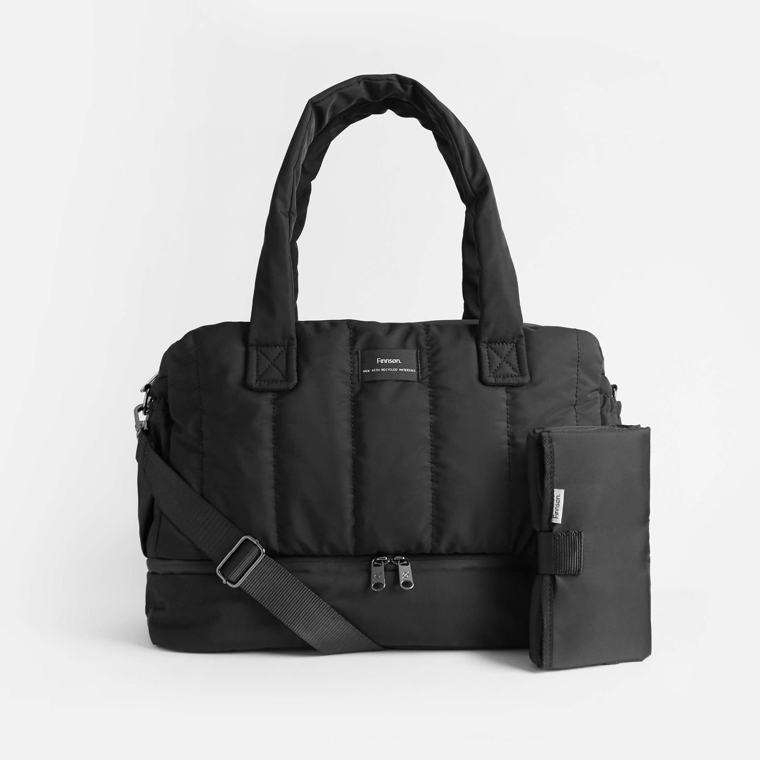 A black INNES quilted changing bag with a changing mat, featuring a zip base compartment, sturdy handles, a crossbody strap, and side D-rings.