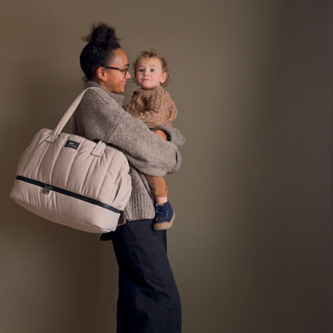 FINNSON INNES HOLDALL TAUPE MOTHER HOLDING CHILD WITH BAG ON SHOULDER