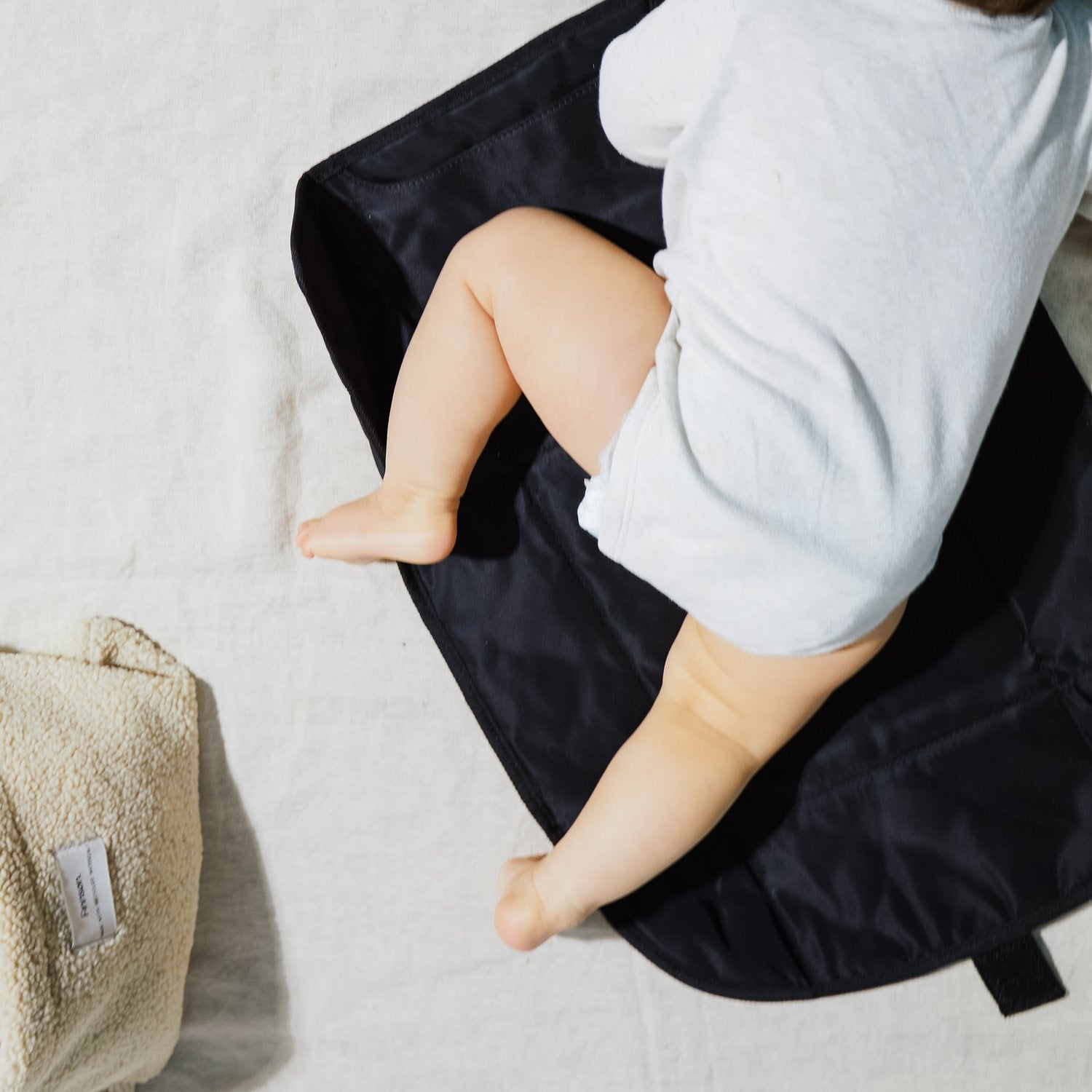 Top-down view of the Kari Black changing mat with a baby lying on the padded surface, showcasing the mat's generous size, quilted finish, and practical design for comfortable diaper changes.