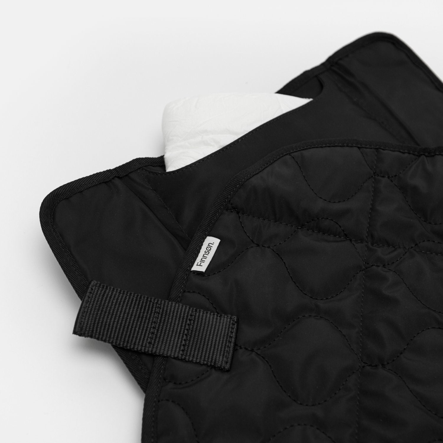 Kari Black changing mat folded with a diaper stored in the built-in pocket, highlighting its quilted design, carry handle, and convenient storage for on-the-go diaper changes.