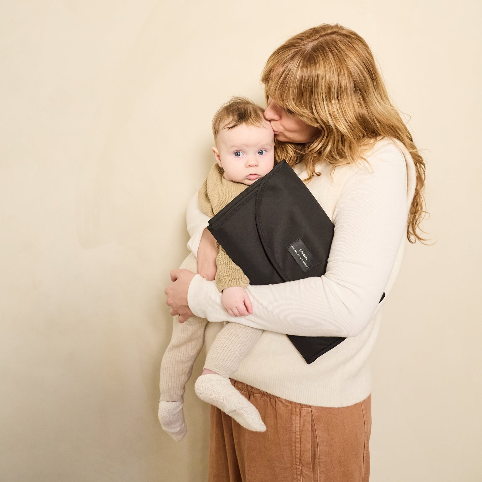 Woman holding a baby and oslo black changing mat against a beige background