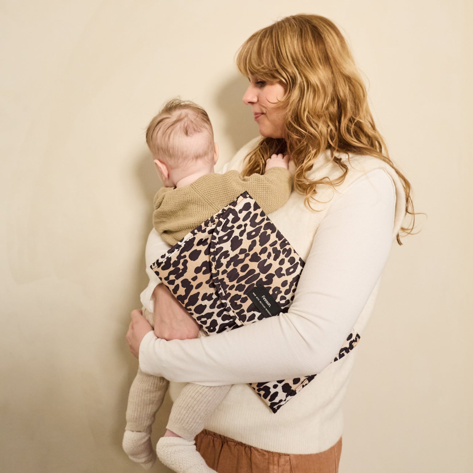 Woman holding a child with Oslo leopard print changing mat against a beige background
