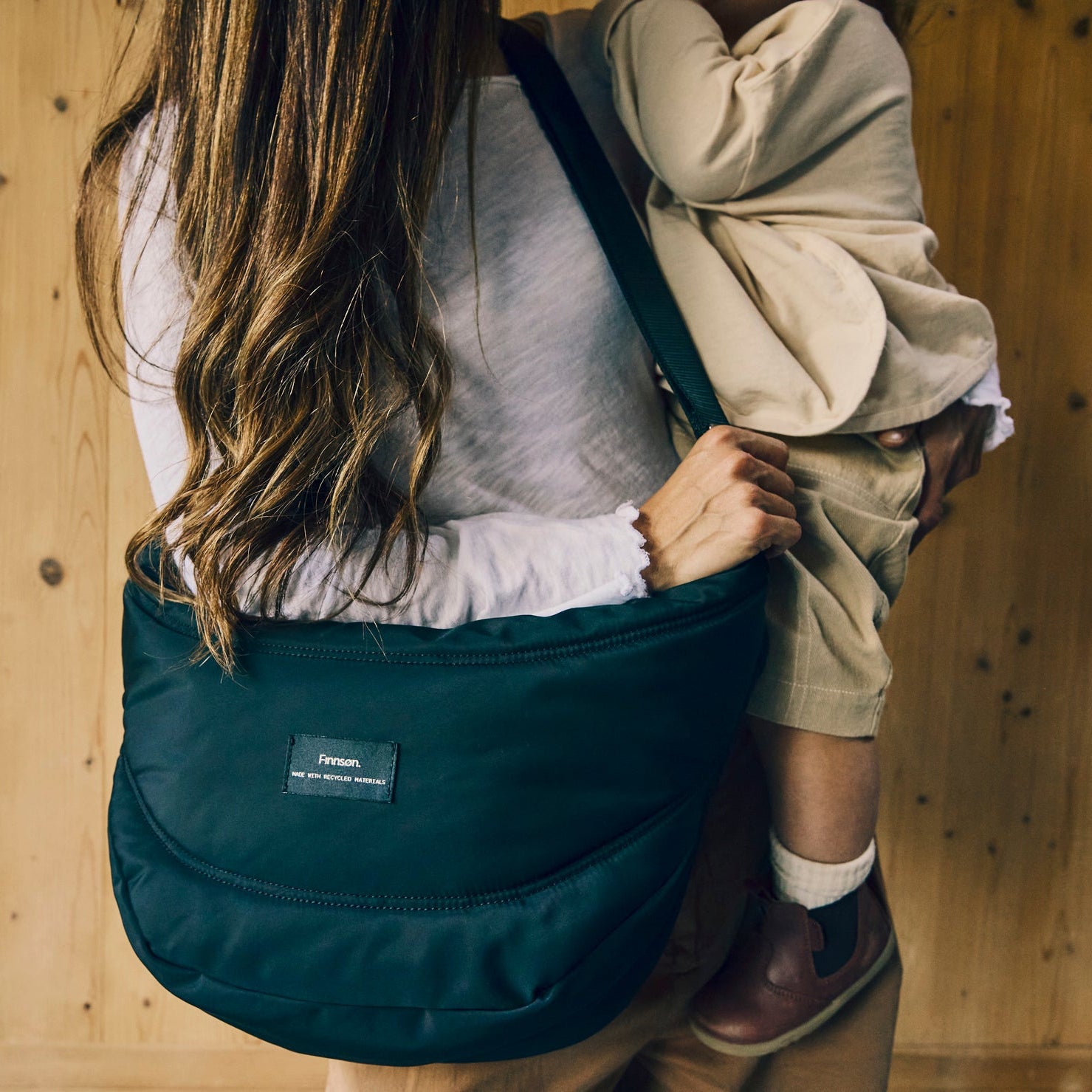 Women holding the Osma stroller organiser black bag with a child on a wooden wall