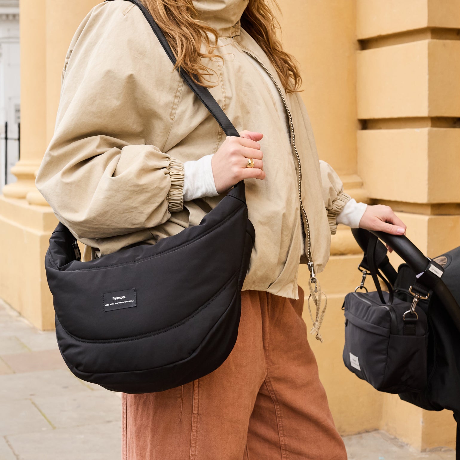 Person holding the Osma stroller organiser black bag and a stroller in an urban setting