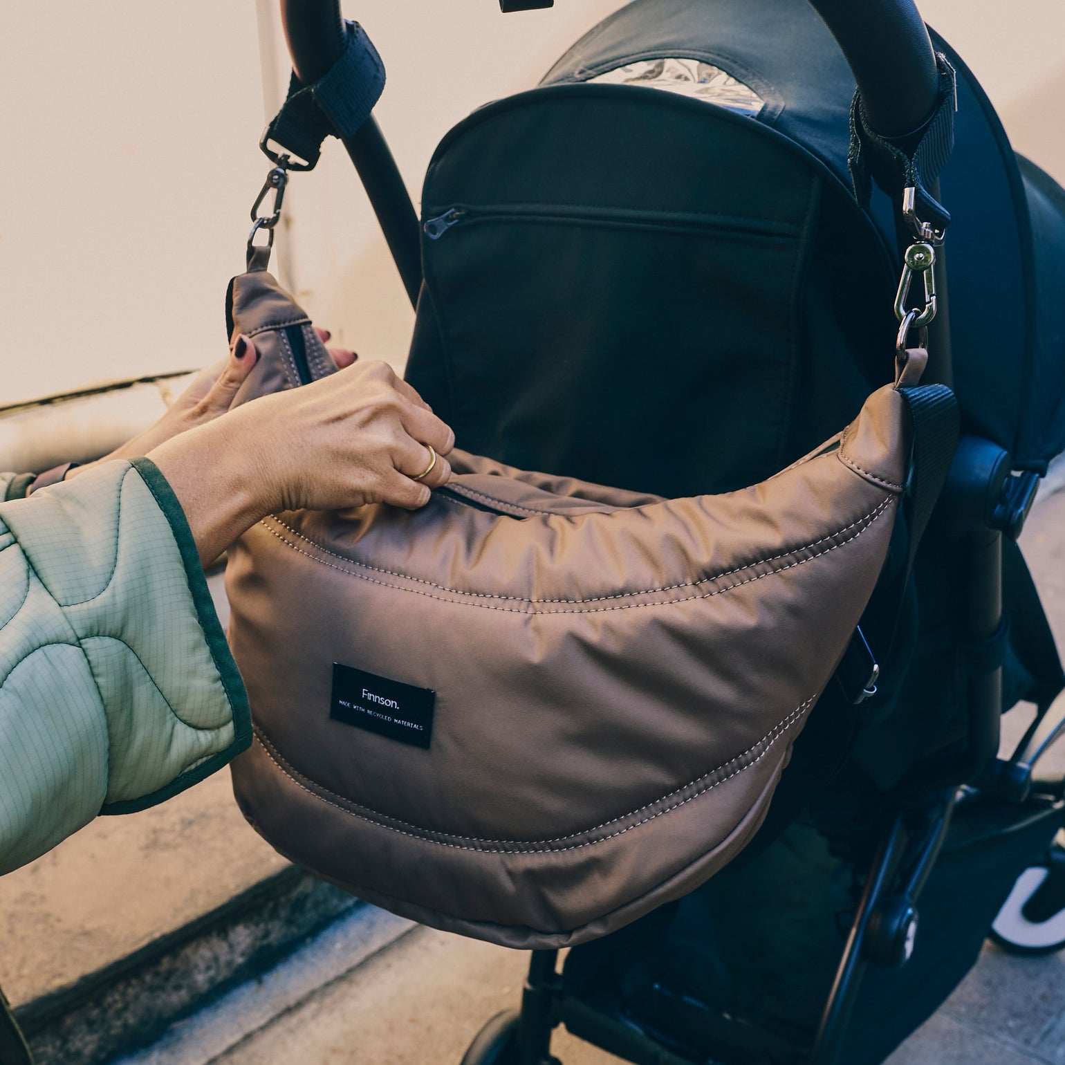 Osma mocha sling stroller orgnaiser attached to a stroller with a blurred background