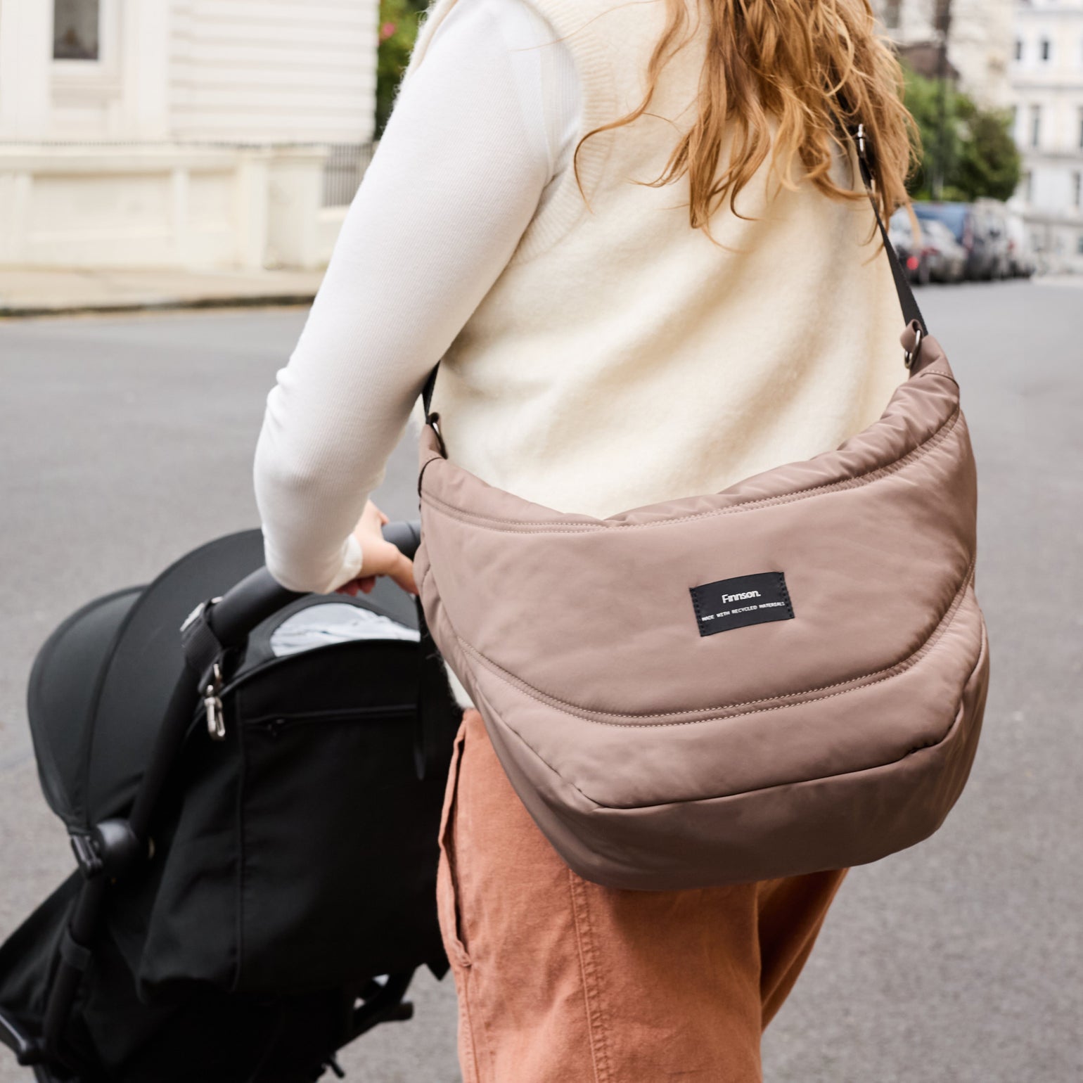 Woman pushing a pram whilst wearing the osma mocha stroller organiser with visible Finnson log 
