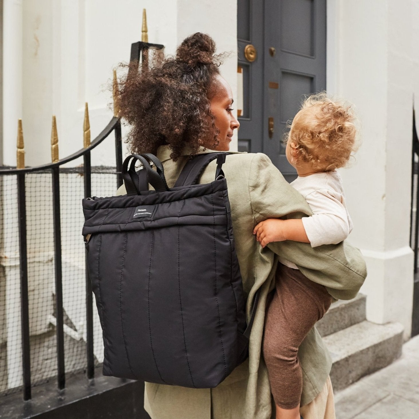 Rae Black Eco Changing Backpack worn by a parent while carrying a child, showcasing its spacious design and practical everyday use for parents on the go.