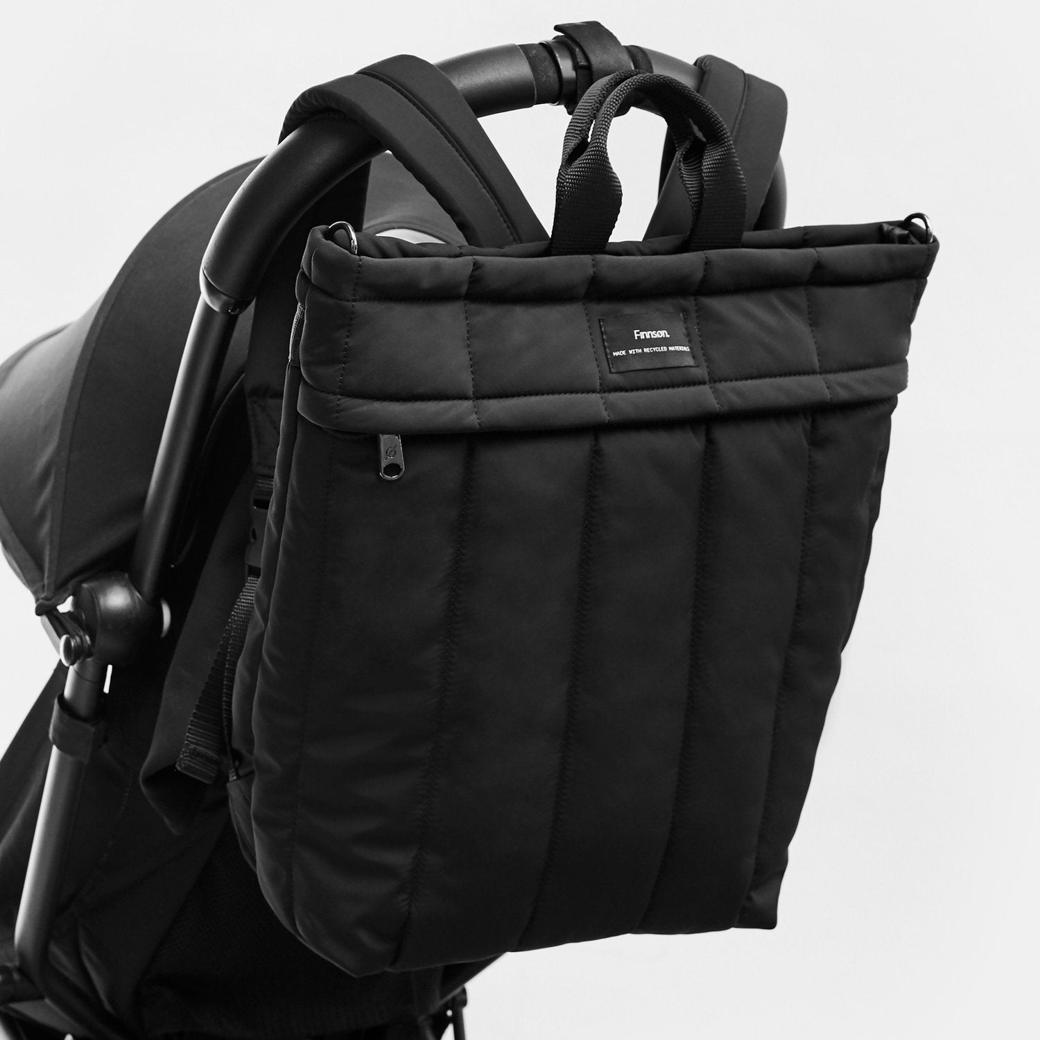 A Rae black Eco Changing Backpack hanging to the pram handle