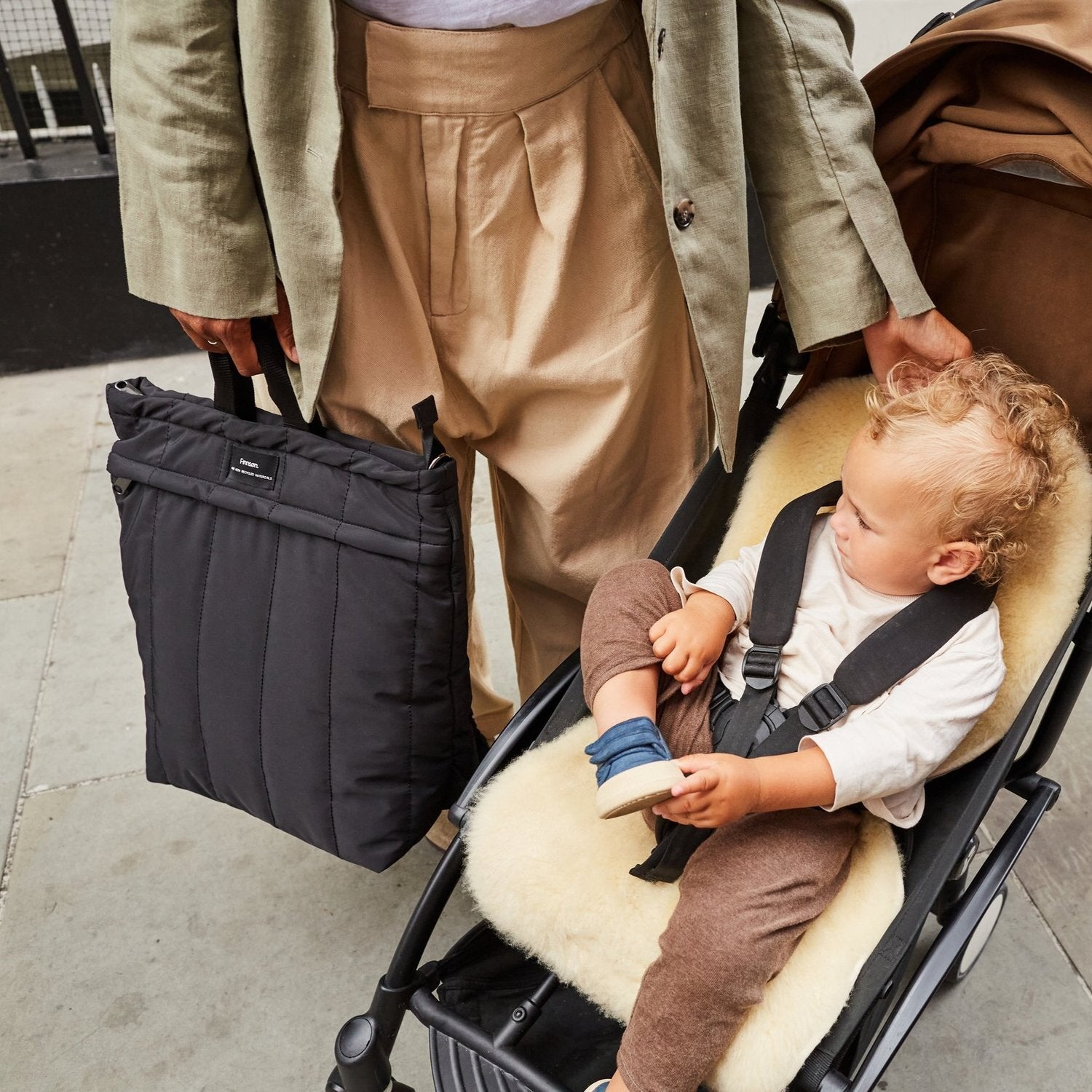 Rae Black Eco Changing Backpack carried beside a stroller, with a child seated comfortably inside, highlighting its convenient design for family outings.