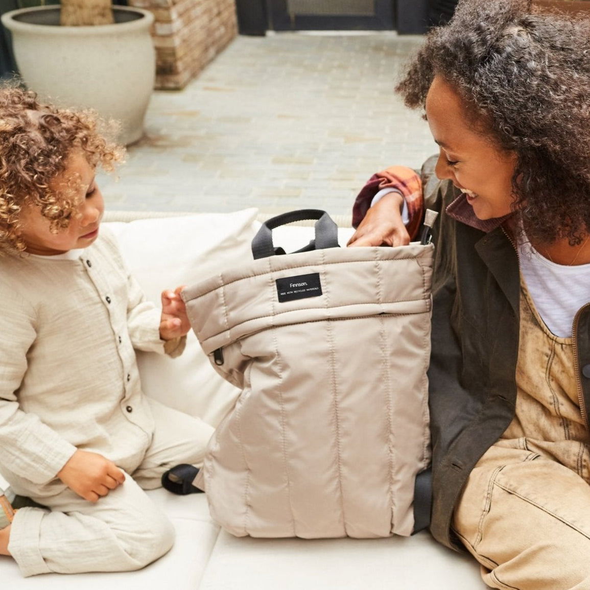 Mom and daughter interacting with a RAE taupe Eco Changing Backpack outdoors.
