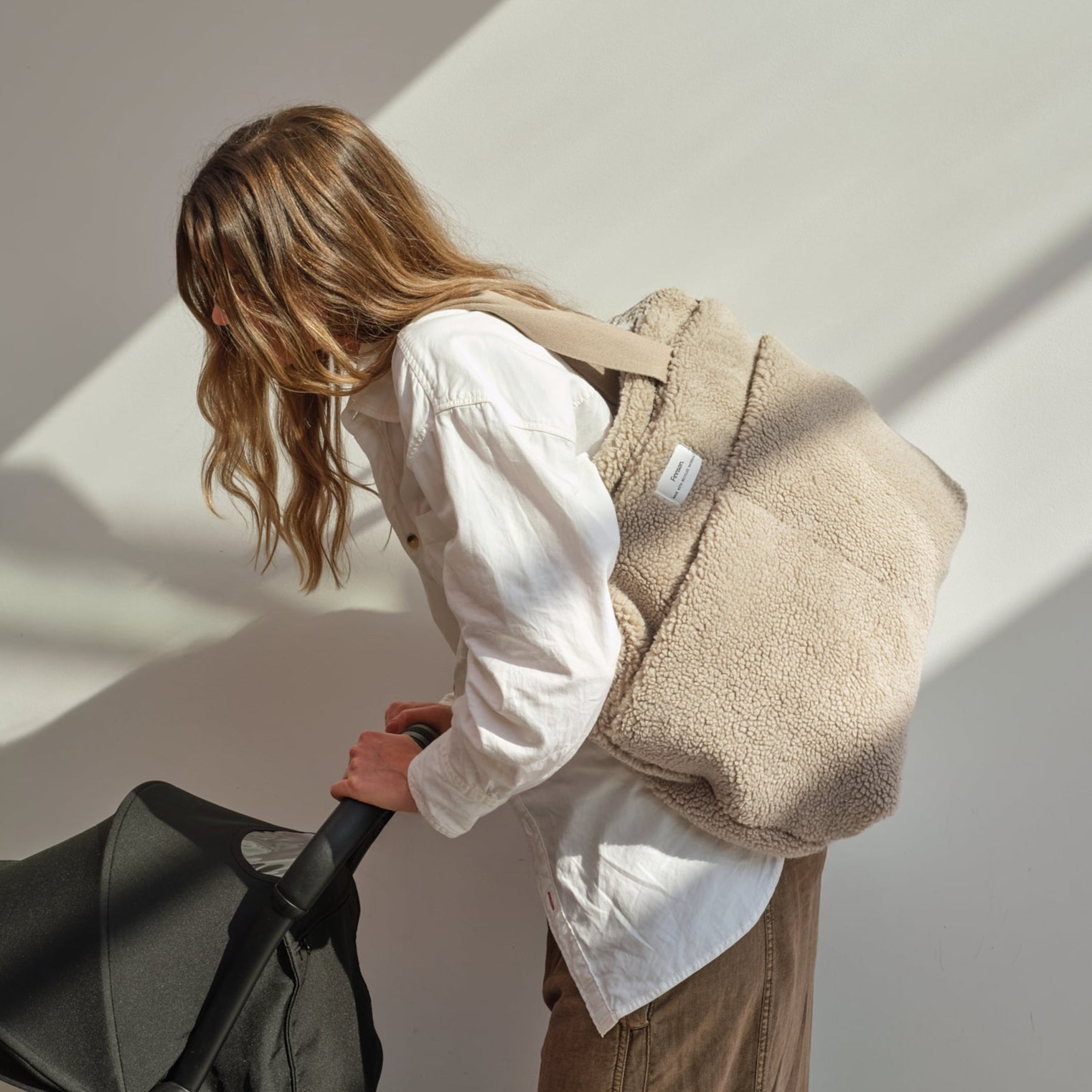 Person with a sigrid mocha borg changing bag holding a black stroller against a white wall.