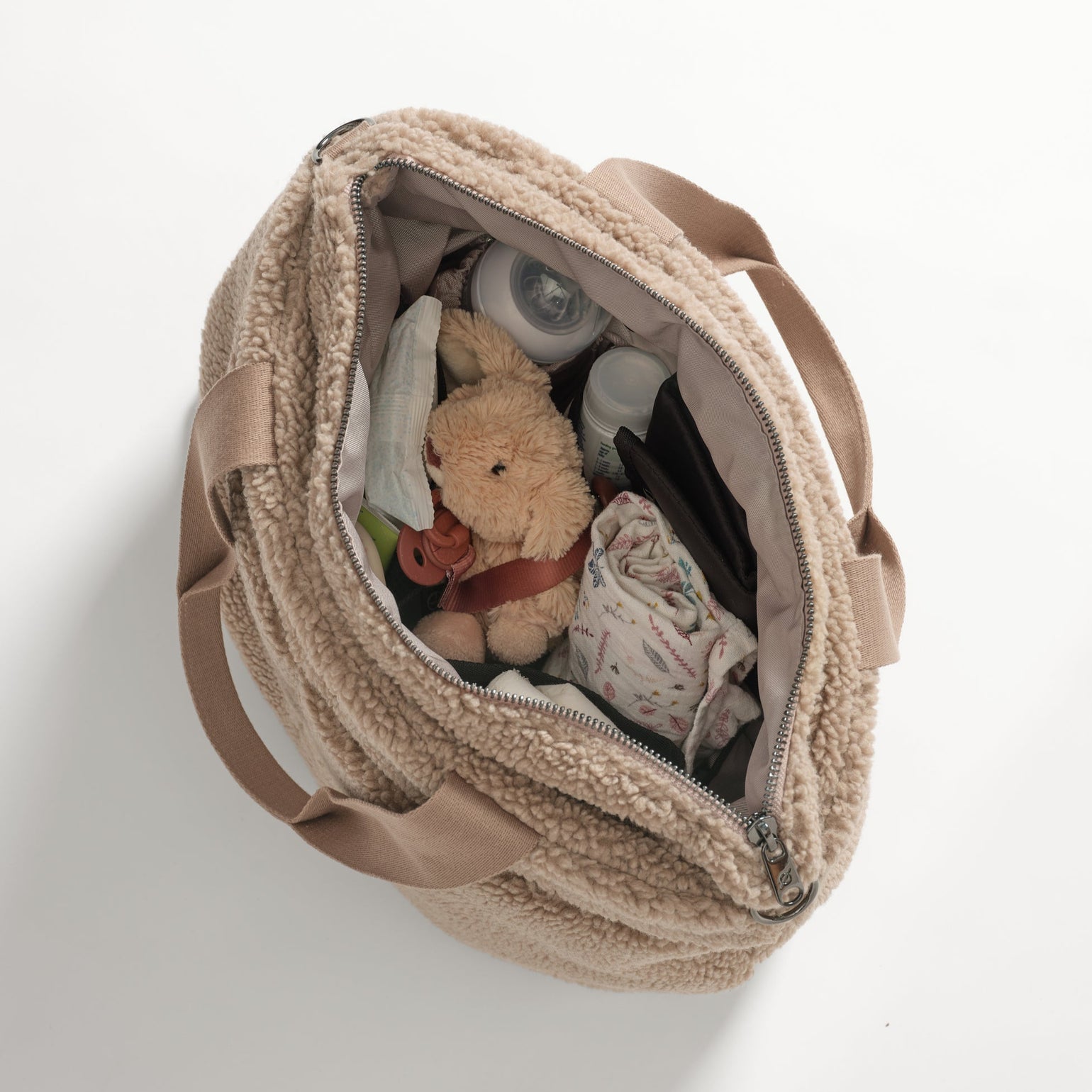 Opened Sigrid mocha borg changing bag with a teddy bear and baby items on a white background