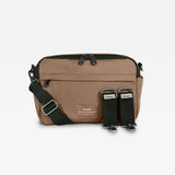 Frida Mocha bag with black accents, featuring a front zip pocket, an adjustable dark green webbing strap, and two black quick-release buckle straps on the front, displayed on a light gray background.