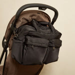 The Iris changing bag with multiple zippered pockets and top handles, shown hanging from the handlebar of a brown stroller against a plain beige wall.