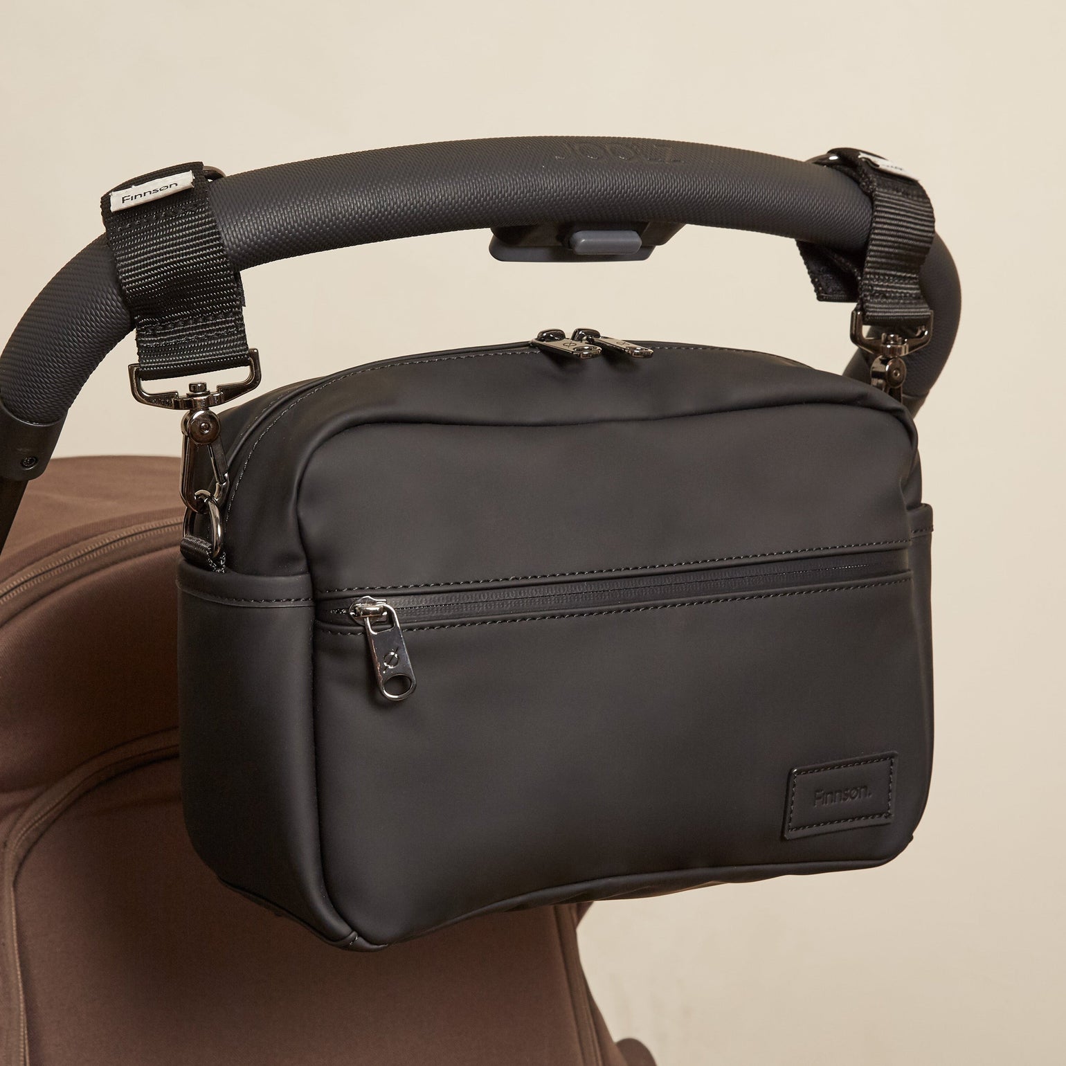 The Fern eco stroller organiser attached to a brown stroller against a plain beige background.
