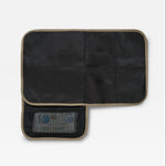 A padded travel changing mat with mocha trim, shown open to reveal multiple interior compartments and a mesh pocket containing toiletry items, on a light gray background.