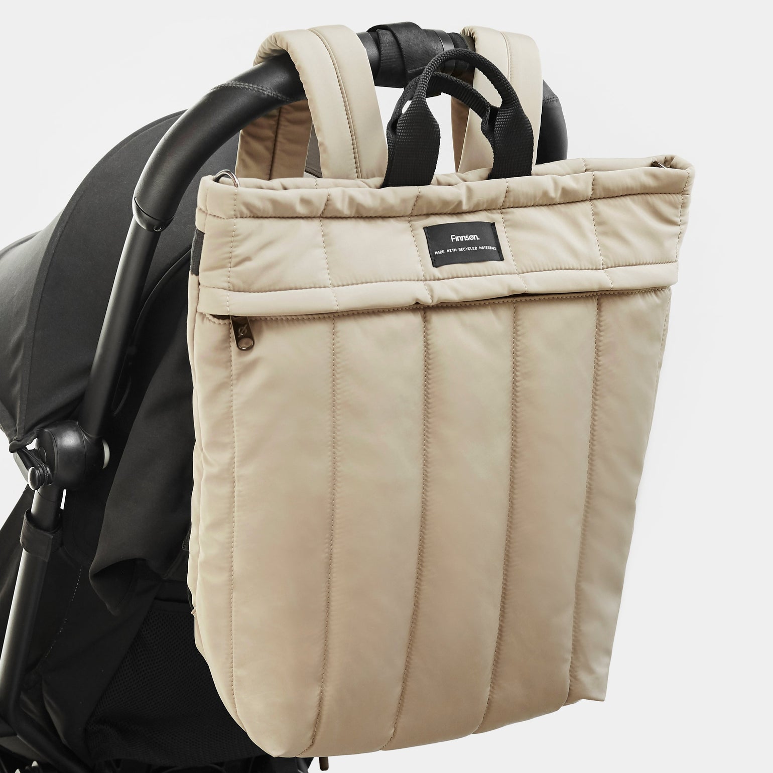 A RAE taupe Eco Changing Backpack hanging to the pram handle