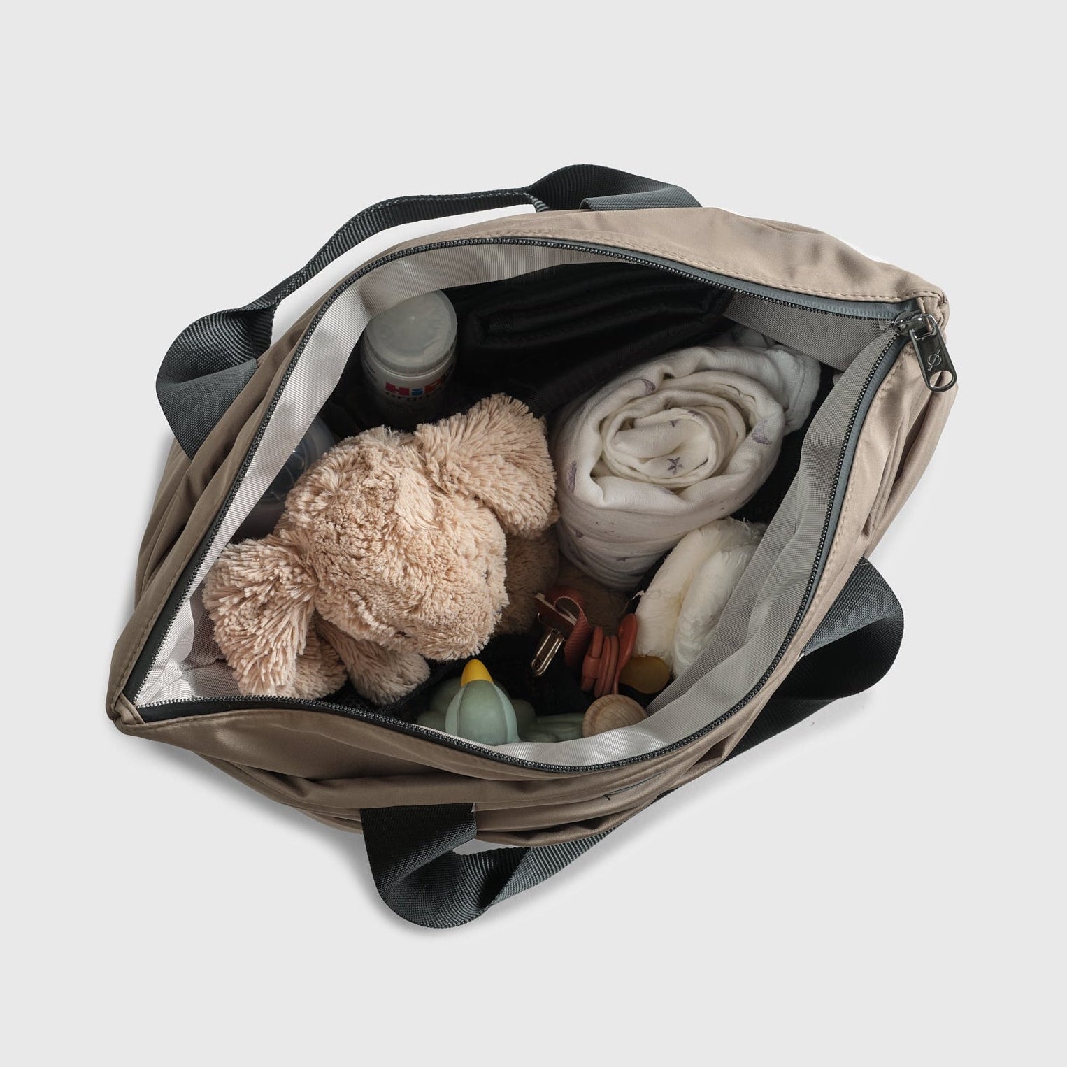 Open Sigrid Eco Stroller Organiser Bag in Mocha containing a teddy bear, bottles, and other items on a light gray background