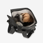 The Finnson Viggo changing backpack in black open from above, revealing a light gray interior with a brown plush toy and other small items inside, on a plain white background.